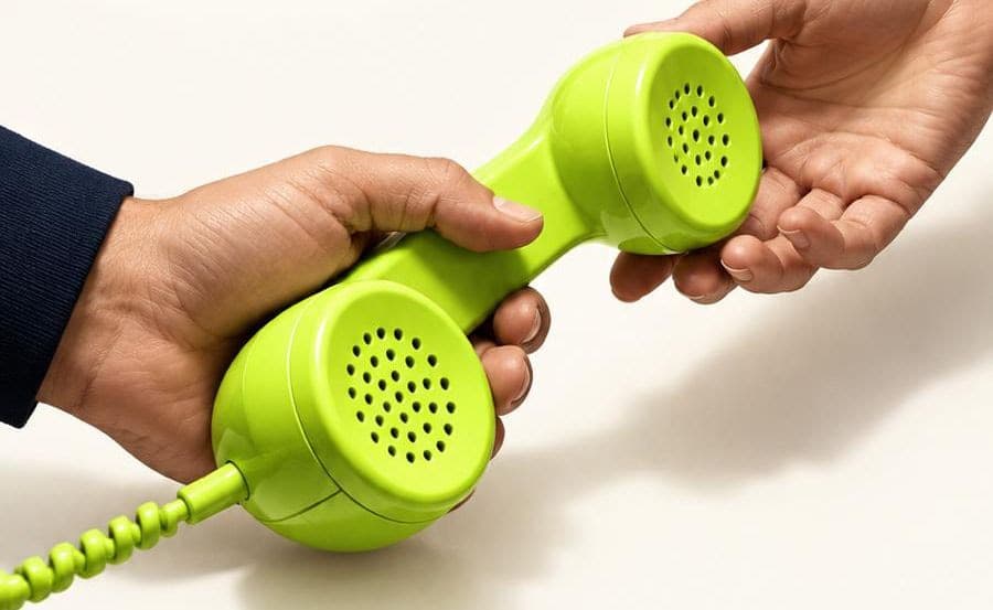 One hand passes a lime-green telephone handset to another